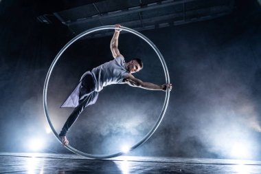 Cyr Wheel sirk sanatçısı dumanlı arka planda, sahnede performans sergiliyor. 