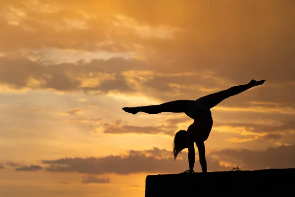 Chica flexible haciendo ejercicio en el fondo del cielo durante el atardecer dramático — Foto de Stock