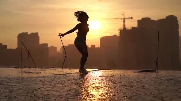 Flexible Turnerin springt akrobatische Split-Tricks mit Spiegelung im Wasser während des dramatischen Sonnenuntergangs an einem regnerischen Tag mit Stadtbild Hintergrund. Konzept von Furchtlosigkeit, Mut und Freiheit — Stockvideo