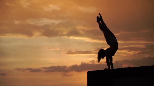 Flexibilní dívka dělá handstand na obloze pozadí během dramatického západu slunce ve zpomaleném filmu — Stock video