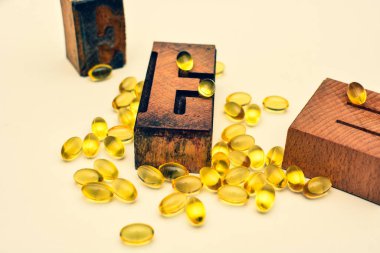 E vitamini yumuşak jel kapsülleri ve ahşap tipografik harf E. Sağlık ve bağışıklık destek konsepti..