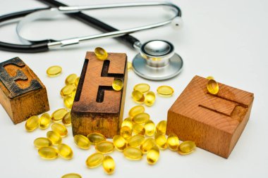 E vitamini yumuşak jel kapsüllü stetoskop ve ahşap basım harfleri E. Sağlık ve bağışıklık destek konsepti..