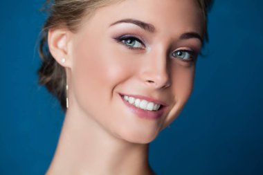 Genç kadın yüzü mavi arka plan, portre portre üzerinde gülümseyen. Sevimli gülümseme