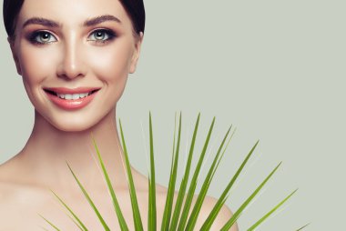 Sağlıklı cilt, sevimli gülümseme ve yeşil palmiye yaprağı ile çekici spa kadın modeli. Yüz tedavi, kozmetik ve spa Güzellik