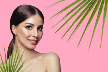 Kopya alanı ile pembe arka plan üzerinde yeşil yaprakları ile genç spa modeli. Spa, sağlık ve cilt bakım kavramı