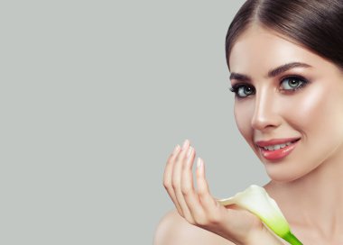Çekici genç kadın yüz portre. Spa modeli ile temiz cilt ve lily çiçekler onun elinde. Yüz tedavi, kozmetik, Güzellik, Cilt Bakımı ve spa