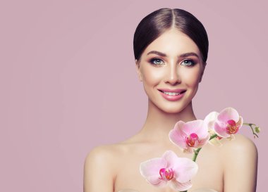 Makyaj ve Pastel pembe bir arka plan üzerinde orkide çiçekleri ile genç gülümseyen kadın