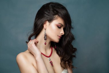 Siyah kıvırcık saçlı ve mavi arka plan üzerinde kırmızı kolye ile genç güzel esmer kadın