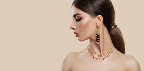 Elegant woman with fashion jewelry on pink background. Gold jewelry for woman, necklace and earrings with black gemstones. Beauty and accessories.