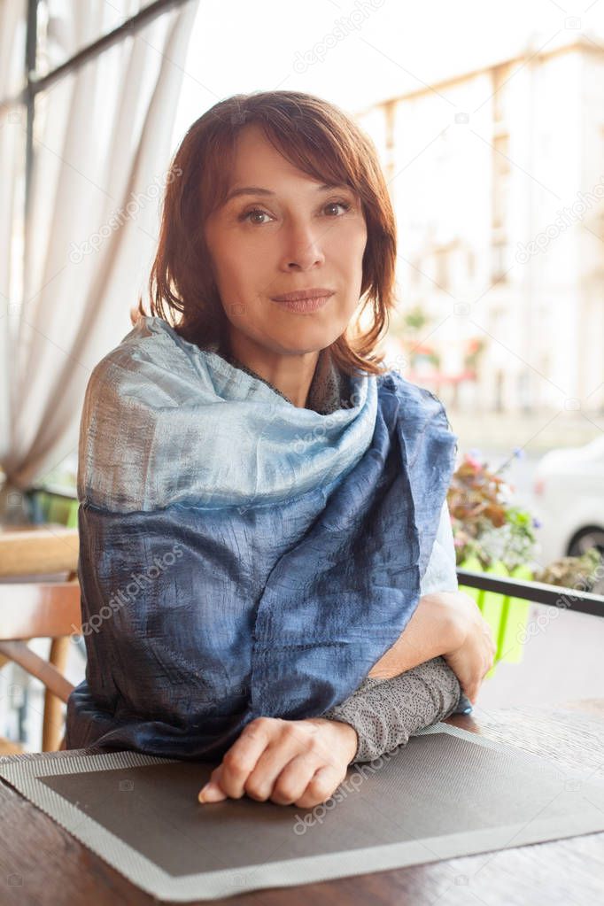 Beautiful mature woman in blue silky scarf sitting in street cafe 