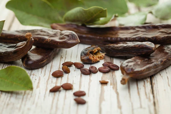 角豆树在白色木桌上放有种子和叶子的豆荚 健康饮食 饮食背景 — 图库照片