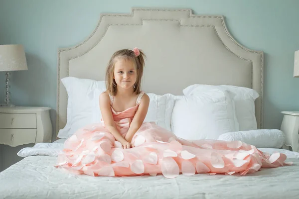 粉红色礼服滑稽的小女孩坐在床上 — 图库照片