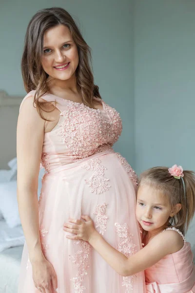 Mutlu bir aile. Anne ve kızı gülümseyerek. Hamile kadın ve çocuk kız