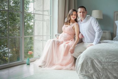 Hamile genç çift birlikte bir pencerede otururken sarılma gülümseyen