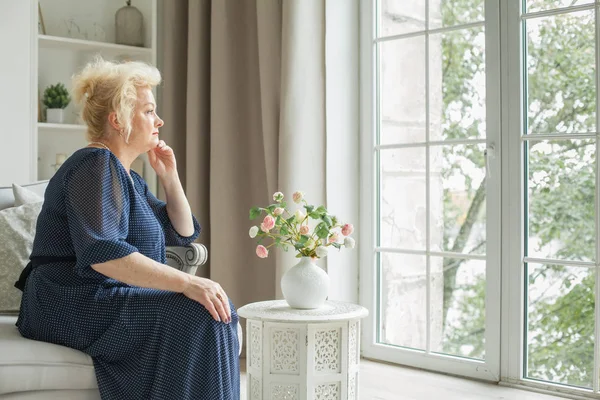 Senior Kobieta Siedzi Kanapie Patrząc Przez Okno Domu — Zdjęcie stockowe