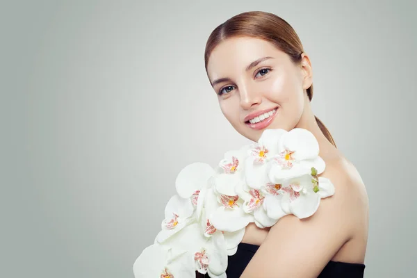 Portrait of happy young woman with healthy skin and white orchid flower. Beautiful girl smiling
