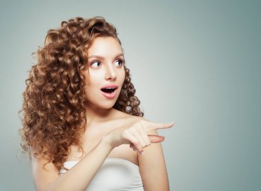 Kadın işaret şaşırttı. Sevimli kadın modeli tarafına işaret uzun kıvırcık saçlı. Ürün sunmak. Olumlu duygu. 