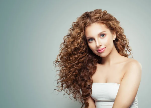 Young friendly woman with long healthy wavy hair on gray background