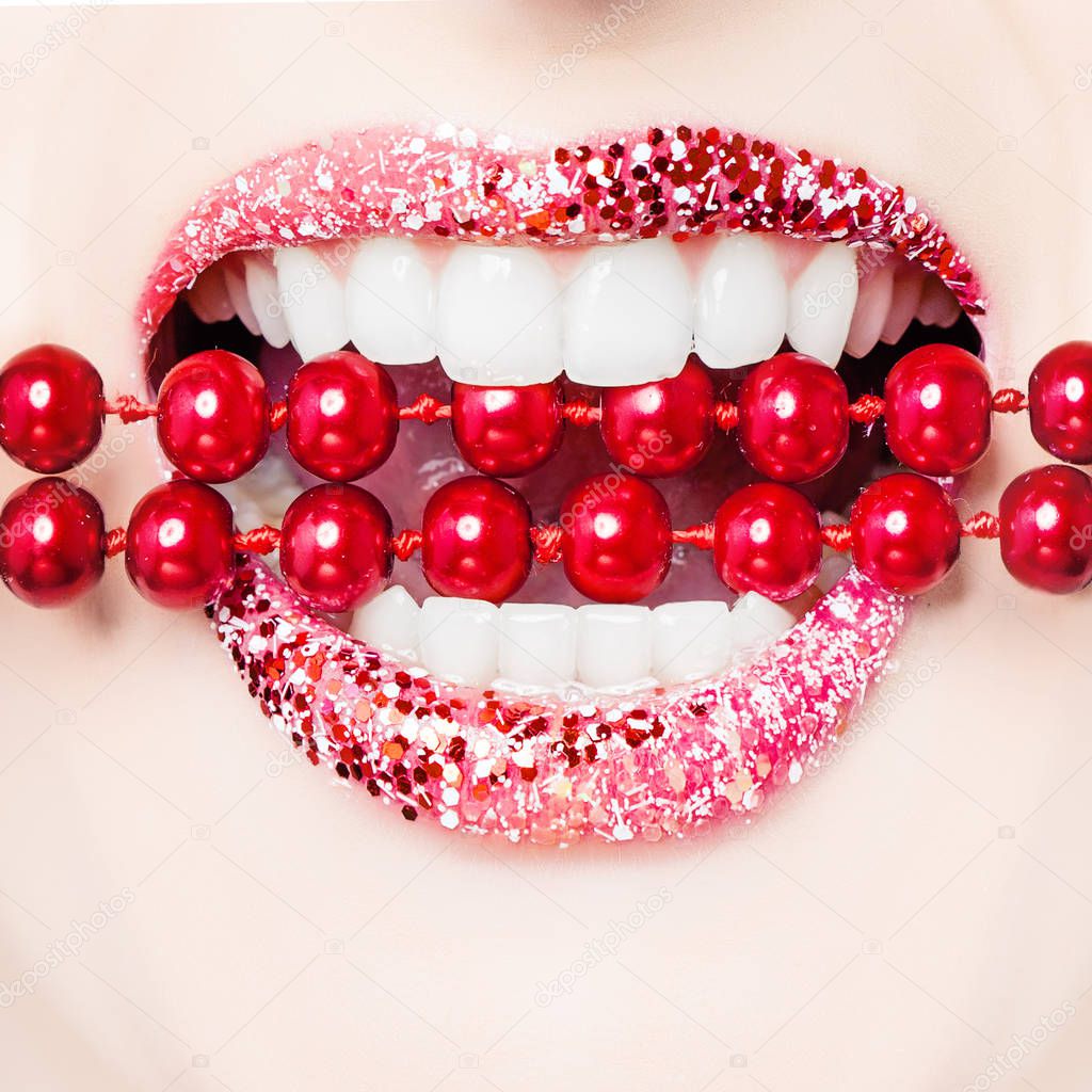 Beautiful female lips with white teeth biting red pearls. Opened mouth with fashionable  glamorous makeup 