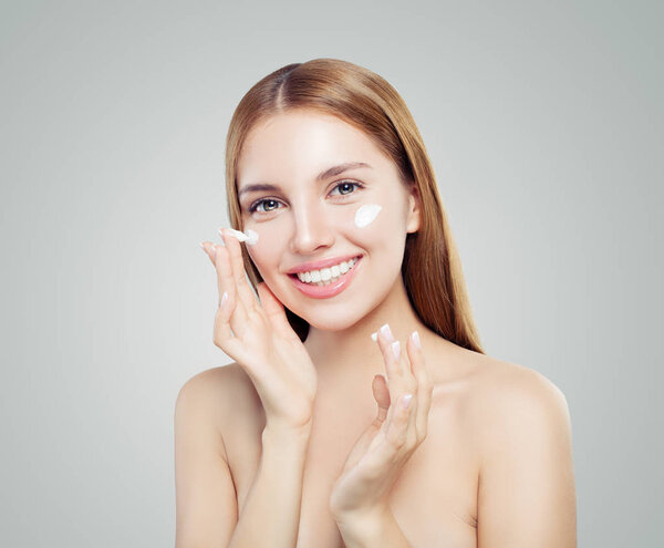 Молодая женщина наносит увлажняющий крем на ее милое лицо на белом фоне
