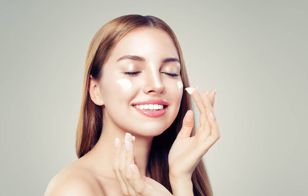 Young woman applying moisturizing cream on her healthy skin. Perfect face closeup. Skin care and facial treatment concept
