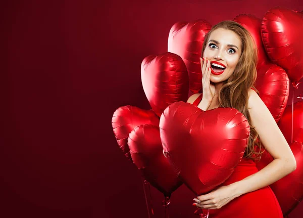 愉快的妇女在红色礼服拿着气球红色心脏在红色横幅背景 快乐的惊喜女孩与红色的嘴唇化妆和可爱的笑容 情人节的人和情人节的概念 — 图库照片