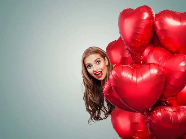 Happy surprised woman withred balloons. Perfect smiling girl with red lips makeup portrait. Surprise, valentines people and Valentine's day banner background with copy space