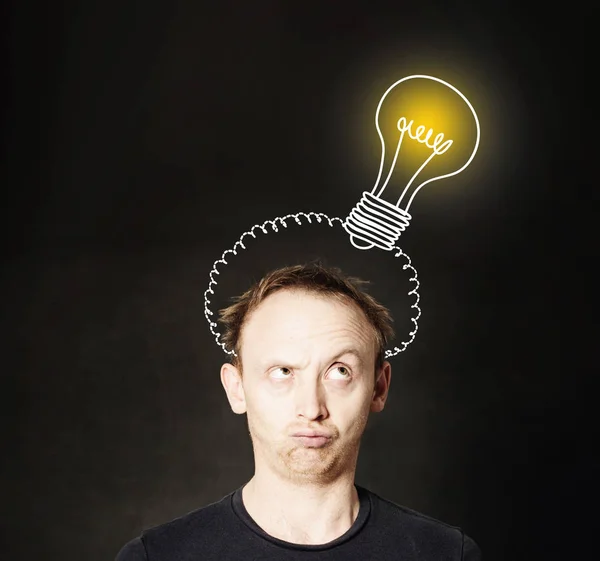 Idea concept. Man thinking on blackboard background with light b