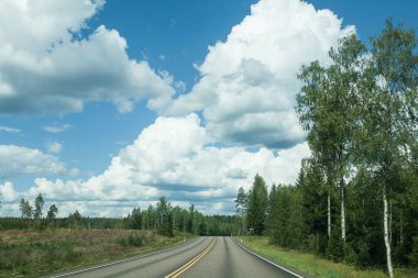 Alanlar, ağaçlar ve mavi gökyüzü ve bulutlar olan yol