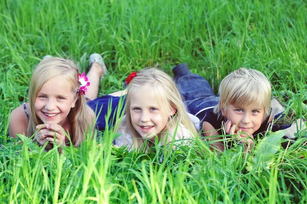 Přátelští děti ležící na zelené trávě v letním parku — Stock fotografie