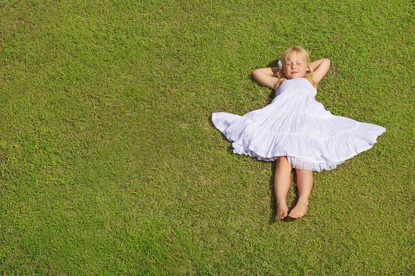 Mooi kind meisje liggend op het groene gras, bovenaanzicht — Stockfoto