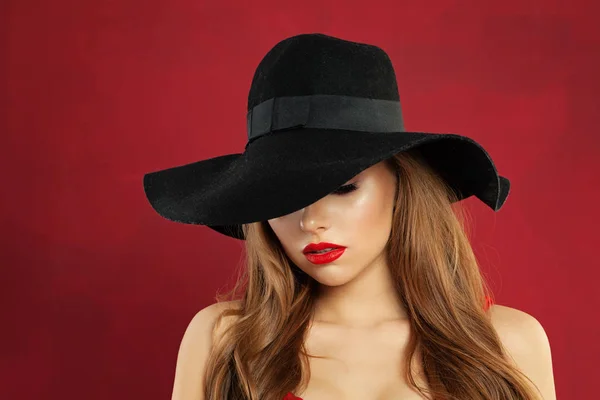 Jolie jeune femme mannequin en chapeau noir sur fond rouge — Photo