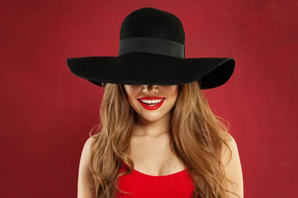Leende kvinna i svart hatt på röd bakgrund. — Stockfoto