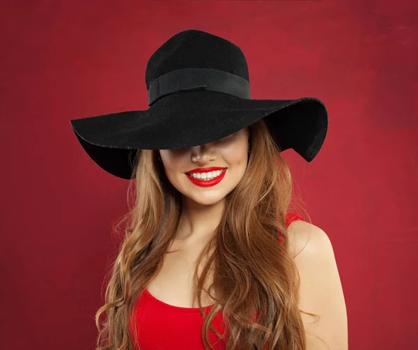 Mujer modelo alegre feliz en sombrero negro sobre fondo rojo . —  Fotos de Stock