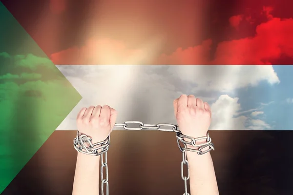Two hands shackled a metal chain on the background of the Sudan flag