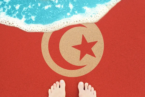 Две ноги на солнечном песчаном пляже с флагом Туниса . — стоковое фото