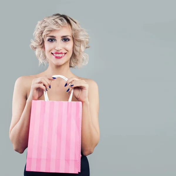 Mujer rubia feliz sosteniendo bolsas de compras rosas y sonriendo — Foto de Stock