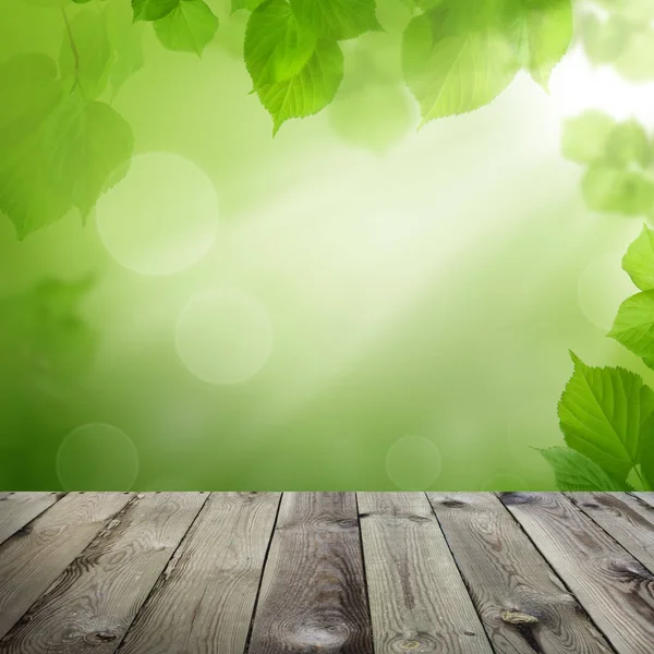 Drewniany stół z zielonymi liśćmi i abstrakcyjnym tłem światła bokeh — Zdjęcie stockowe