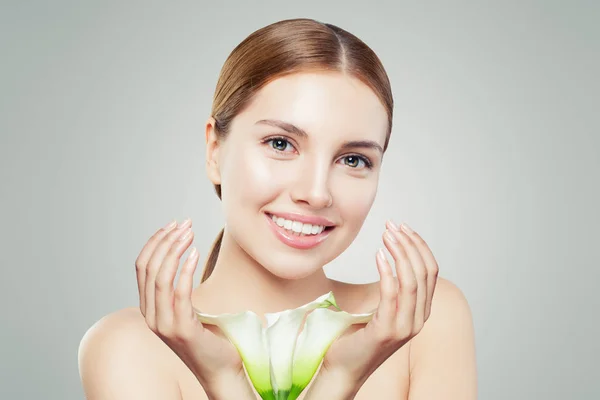 Beautiful young woman with clear skin and flowers on gray — Stock Photo, Image