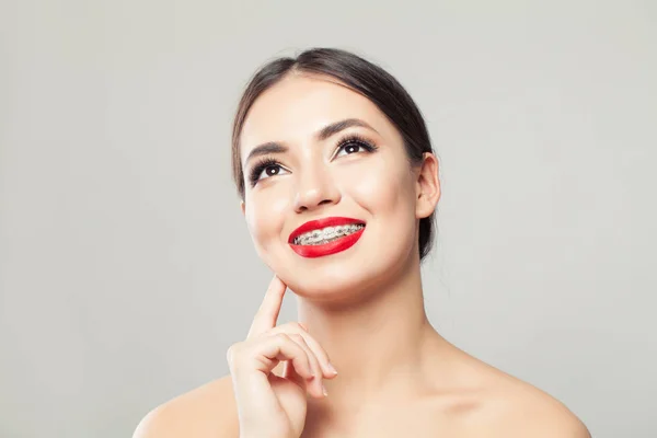 Jovem mulher em aparelho sorrindo e olhando para cima no fundo branco — Fotografia de Stock