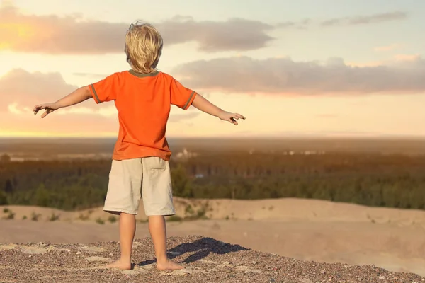 Niño de pie y mirando el atardecer en la montaña de arena —  Fotos de Stock
