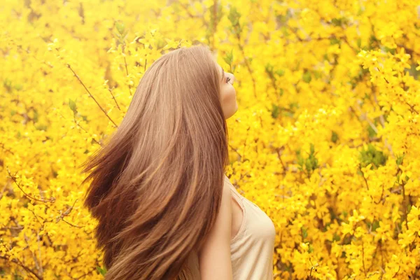 Mulher bonita com cabelo longo e saudável contra fundo flores amarelas. Menina com sopro penteado retrato — Fotografia de Stock
