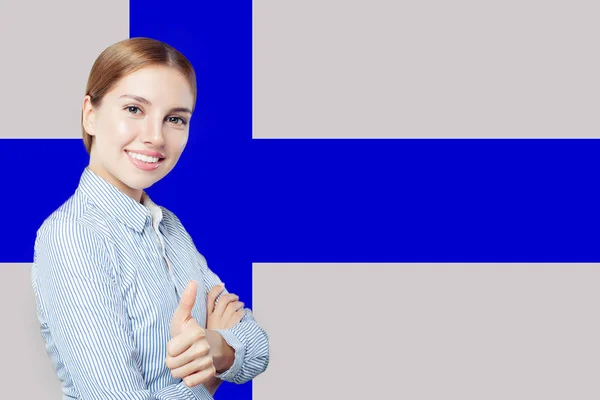 Финляндия. Молодая счастливая милая девушка с большим пальцем на фоне финского флага — стоковое фото