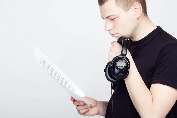 Jonge man met koptelefoon kijk op de muziek notities — Stockfoto