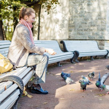 Güzel kadın parkta dinleniyor ve güvercinleri besliyor