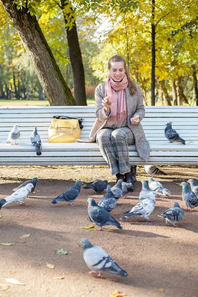 Mujer bonita descansando en el parque y alimentando palomas —  Fotos de Stock