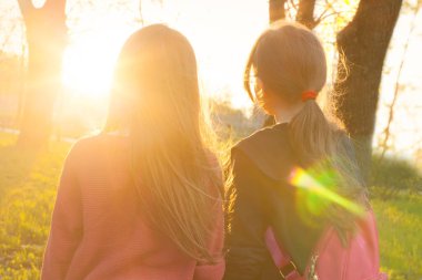 Parkta gün batımına bakan iki kız çocuğu el ele tutuşuyorlar.
