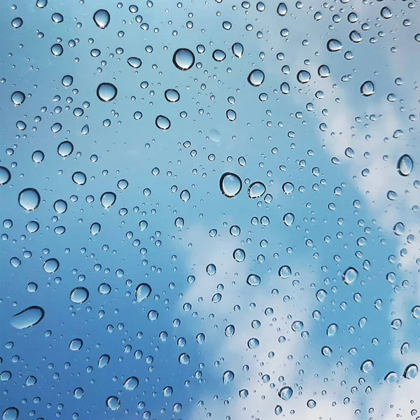 Waterdruppels op glas met blauwe lucht en wolken achtergrond. — Stockfoto