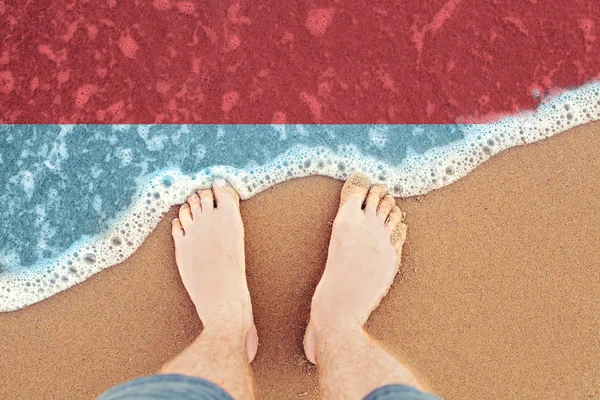 Feet on sandy beach with flag Indonesia. Top View on sea surf. — Stock Photo, Image
