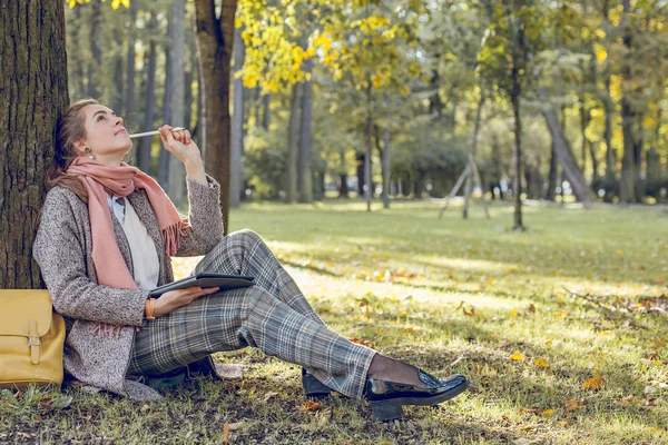 Mooie vrouw met tablet laptop zittend op groen gras, werken en ontspannen in het park buiten — Stockfoto